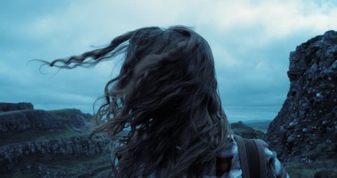 Close up portrait of Young Woman hiker exploring nature with hair blowing in wind Hiker Girl trekking in cold stormy weather Quiraing Scotland Slow Motion