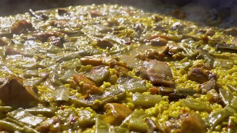 Cooking authentic Valencian paella with chicken meat, rabbit meat, vegetables, boiling Valencian rice, saffron. Typical cuisine of the Valencia Spain. Boiled bubbles in slow motion