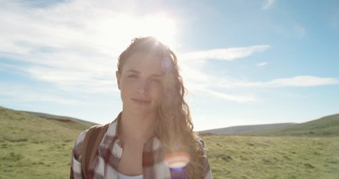 Close up portrait of Beautiful Young Woman Smiling in nature with hair blowing in wind Hiker Girl standing in front of sun flare trekking in Scotland Slow Motion
