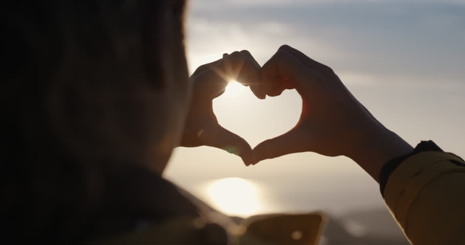 Beautiful Woman making heart shape with hands at sunset Girl holding up love symbol gesture with orange sun flare