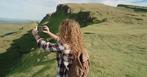 Hiker Woman taking photo smartphone photographing scenic landscape nature background view Hipster girl enjoying vacation travel adventure. Quiraing Walk on the Isle of Skye in Scotland