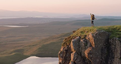 Woman dancing silly freestyle dance outdoors standing on cliff edge at sunrise Crazy dancer girl having fun enjoying nature celebrating vacation travel adventure Scotland