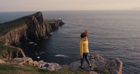 Woman dancing silly freestyle dance on ocean cliff outdoors at sunset Crazy dancer girl having fun enjoying nature celebrating vacation travel adventure Neist Point Lighthouse Scotland
