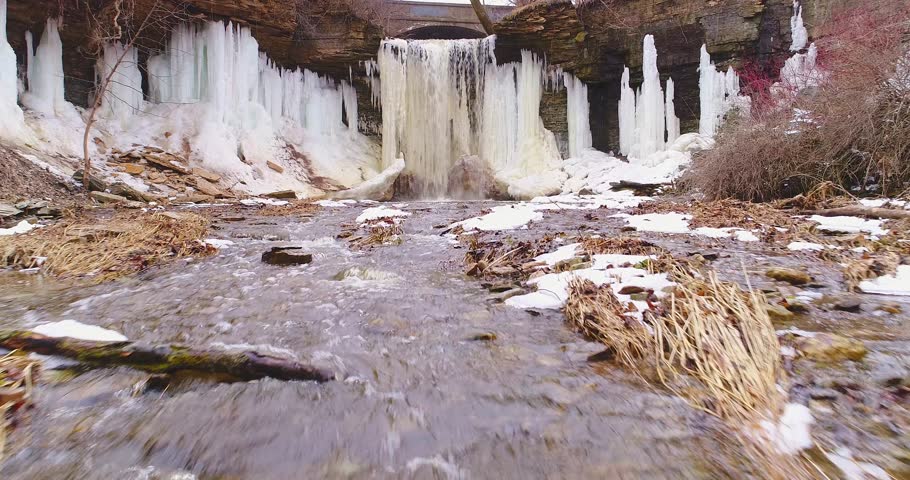 Breathtaking low aerial footage of frozen waterfall, thawing in Springtime, with beautiful ice sculptures carved by nature. This is Wequiock Falls near Green Bay, Wisconsin.