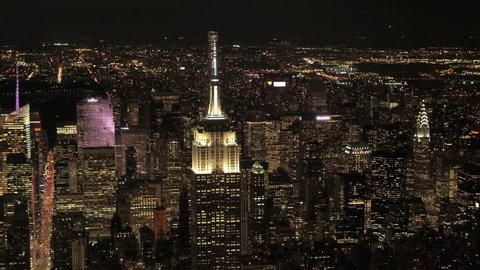 AERIAL HELI SHOT, NO VISIBLE TRADEMARKS Upper Manhattan & Queens borough behind lit up with lights Empire State and Chrysler building. Magical city lights in stunning New York skyline on summer night