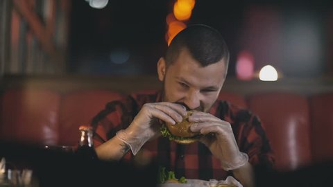Man in gloves is eating a burger