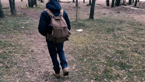 Camera chases the person and takes off as he walks with a backpack in the forest. Slow motion video back view.