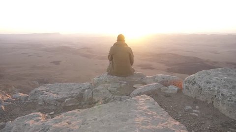 Man is sitting and looking at the sunrise of the desert