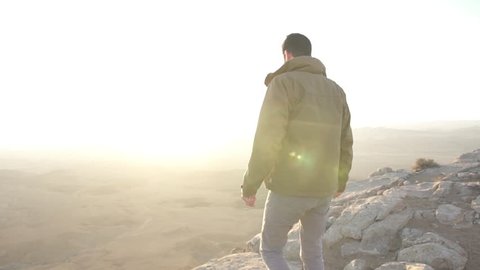 Man walks over to the edge of a desert cliff in the morning