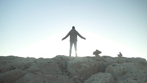 Man standing on the edge of a desert mountain with his arms open