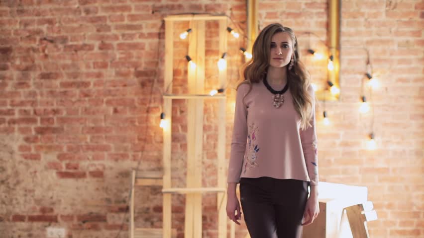Young stylish woman posing against old brick wall. Girl defile in the loft interior
