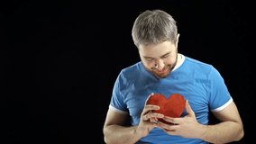 Smiling bearded man in blue tshirt holds two red heart shapes. Love, romance, dating, relationship concepts. Black background. 4K video