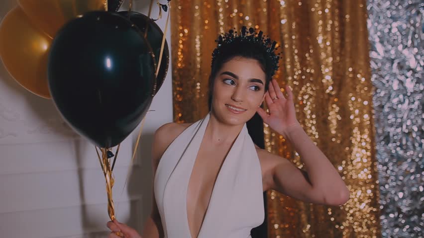 Young girl in white dress with crown. Gold background, balloons