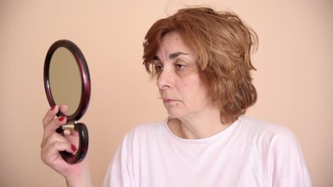 Unhappy and unsatisfied middle aged woman looking at her skin in the mirror