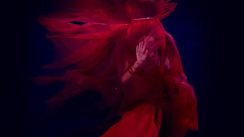 Slow motion dancing girl artist under water. For a red cloth to the light with his hands and face.