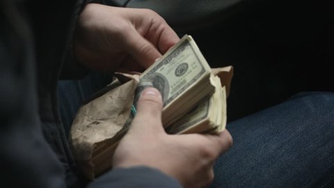 View from over shoulder of man pulls from the package large sum of money sitting behind the wheel of car, close up shots