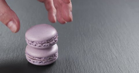 Slow motion of man hand stacking lavender violet macarons on slate board, 4k 60fps prores footage