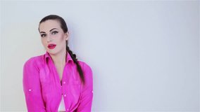 Video footage beautiful young girl with long braid in pink shirt. Girl in pink plump lips with bright makeup poses positively on the camera,smiling,having fun,making kisses,touching her hair,winking.