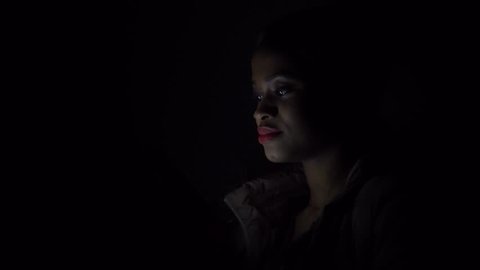 Black lady talks on her smartphone in the darkness