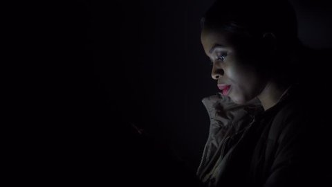 Black woman reads something in her smartphone standing in the darkness