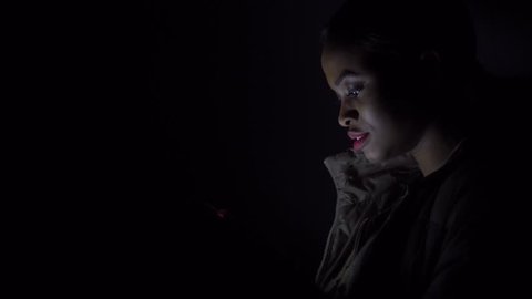 Black woman checks her phone in the darkness