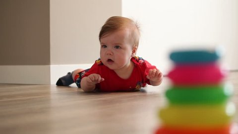 Baby Girl With Blue Eyes And Blonde Hair Is Yawns And Tries  Crawling. Colored Pyramid  In The Foreground.