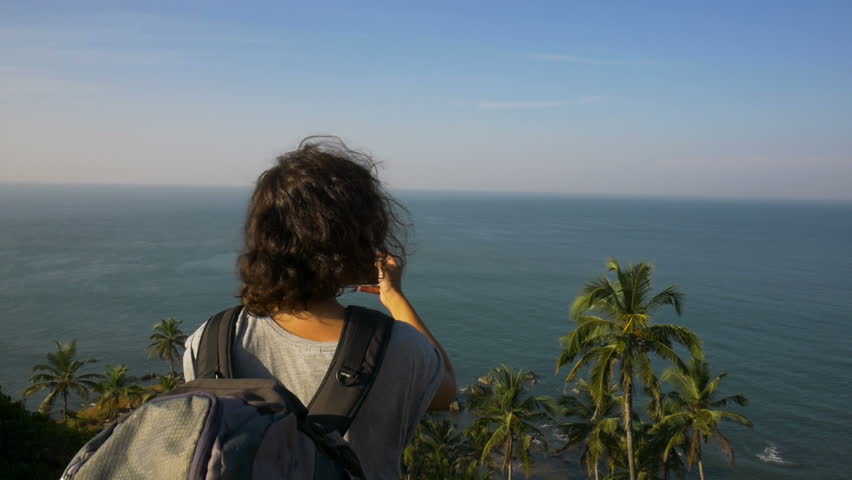 Young woman backpacker taking photo with cellphone on mountain peak