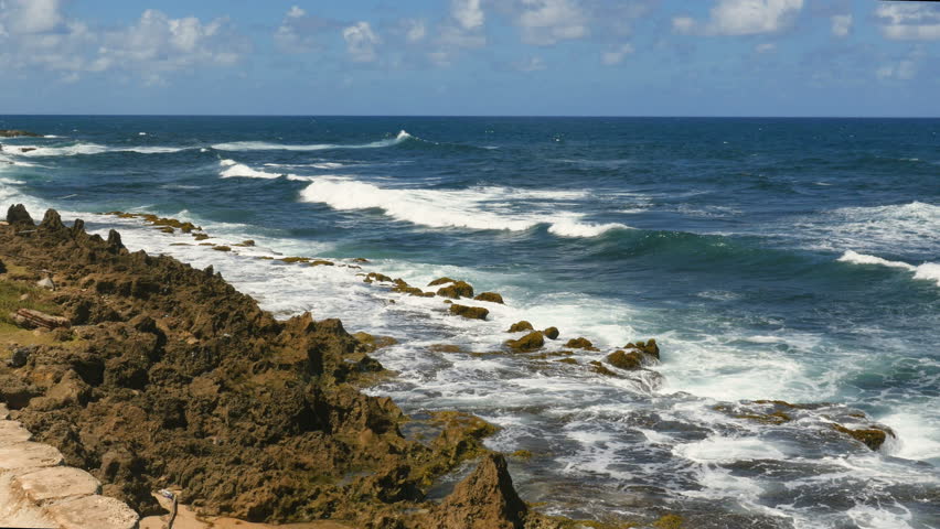 Waves roll onto rocky shore line on the Puerto Rico north shore with blue sky and clouds