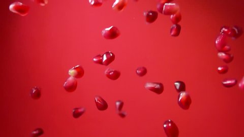 Ripe garnet seeds fly on a red background in slow motion