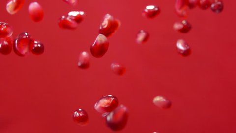 Red ripe garnet seeds fly on a red background in slow motion
