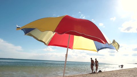 Beautiful bright umbrella flew away from a gust of wind. Beach season. Funny colorful beach umbrella. People bathe in the sea.