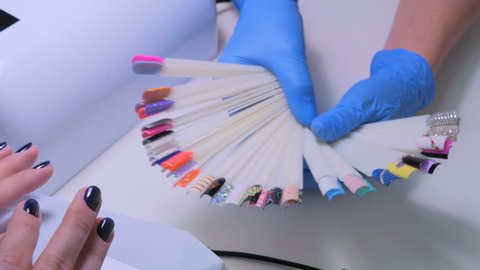 Nail technician shows the color palette of nail services in beauty salon. Woman selects of nail design.