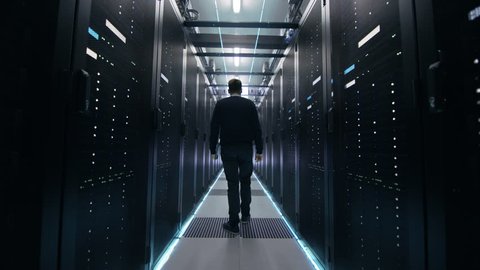 Following Shot of IT Engineer Walking Through Data Center Corridor with Rows of Rack Servers. Opens Laptop. Shot on RED EPIC-W 8K Helium Cinema Camera.