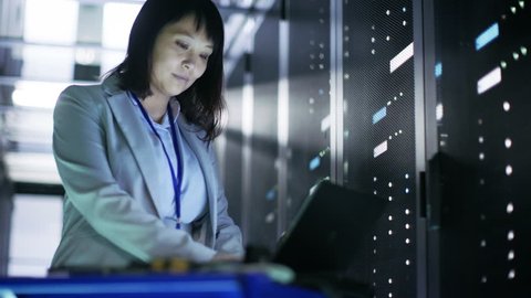 Asian Female IT Engineer Working on a Crash Cart Laptop, She Scans Hard Drives. She's in Big Data Center Full of Rack Servers. Shot on RED EPIC-W 8K Helium Cinema Camera.