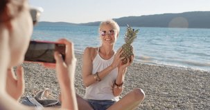 Close up attractive woman holding up pineapple posing for camera smiling laughing at sunset on tropical beach