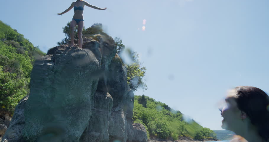 Young woman jumping into clear blue water swimming in lake on bright sunny summer day enjoying nature outdoors