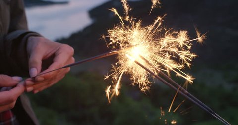 Best friends holding sparklers dancing in slow motion celebrating new year's eve and independence day with fireworks at sunset