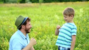 Portrait of happy caucasian family of two people having fun outside in summer green field. Dad plays with his little funny sun. Real time full hd video footage.