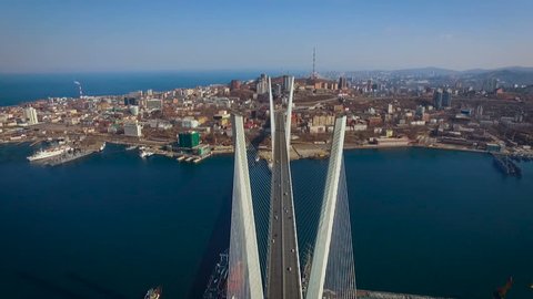 Vladivostok City. Zolotoy Rog Bay Bridge. Top Construction View. Cars on Road Riding Below. Hills on Horizon. Ships by Shore. Small Houses. Wide Shot