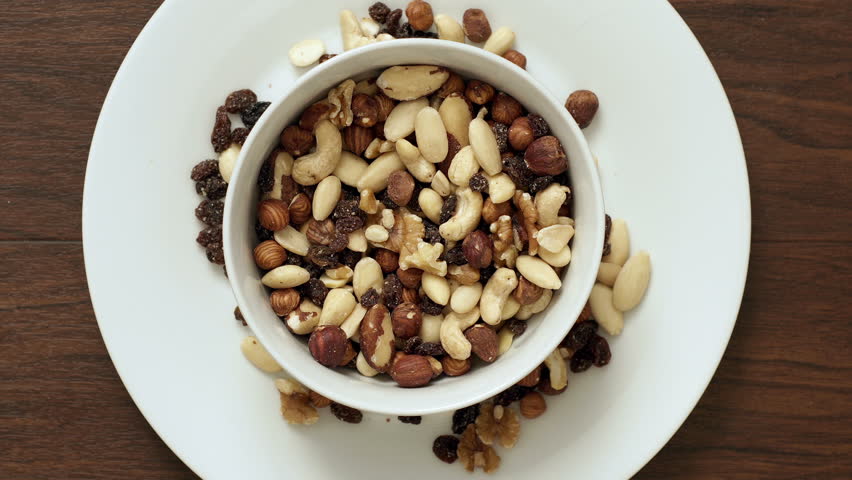 A closeup shot of a couple eating a bowl of mixed nut and raisins trail mix which is a healthy vegetarian snack.