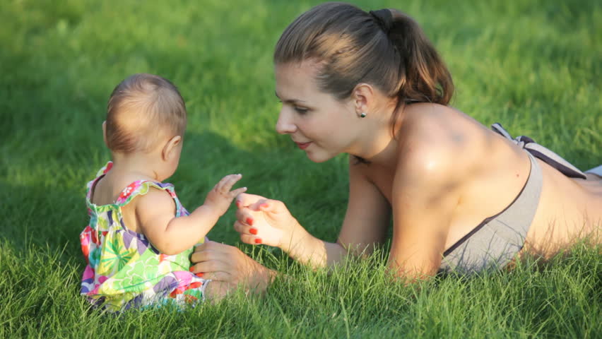 young woman lying in the grass and talking with her baby