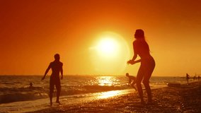 Young couple playing volleyball on the summer beach at sunset