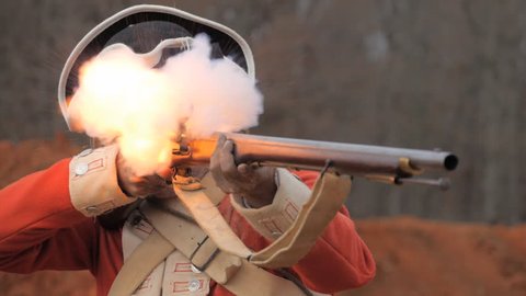VIRGINIA - OCTOBER 2016 - American Revolution era British Redcoat Soldier. Re-enactors, reenactment.  Firing Brown Bess musket gun with black powder and lead bullets in earthen fort in battle. 
