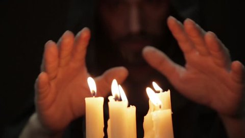 man doing the magic ritual. close-up several candle and old book. necromancer casts spells from thick ancient book by candlelight