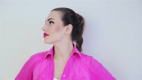 Video footage beautiful young girl with long braid in pink shirt. Girl in pink plump lips with bright makeup poses positively on the camera, smiling, having fun,making kisses, winking.
