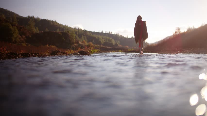 Young redhead hipster crossing mountain river and playfully splashing water at camera
