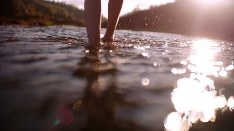 Close up of woman's legs walking barefoot in mountain river and connecting with nature