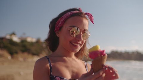 Young brunette woman eating ice cream, walking on beach and looking at the beautiful view