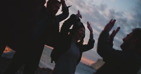 Cool young hipster friends doing high five and having fun on a beach at sunset