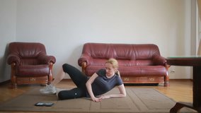 A housewife woman does fitness exercises for the first time, looking at the tablet and TV, it is difficult and unfamiliar, she is tired.